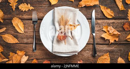 Sfondo autunnale con posate, piatti e foglie autunnali su sfondo ligneo. Foto Stock