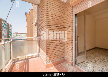 Piccola terrazza vuota con mattoni a vista, pavimenti in argilla e ringhiera metallica e vetro traslucido e accesso ad una stanza con porte in alluminio e vetro Foto Stock