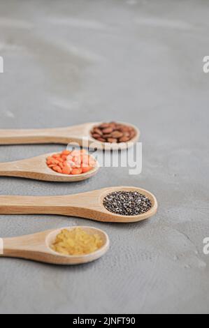 Diversi o vari tipi di fagioli secchi o legumi secchi in cucchiaio di legno su sfondo grigio. Grani interi, alimento sano e concetto di dieta Foto Stock