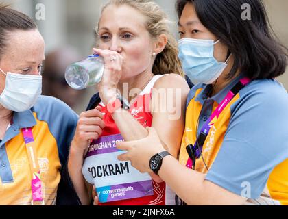 Un esausto Natasha Cockram, Galles, è assistito da medici dopo il 12th in arrivo nella maratona femminile ai Giochi del Commonwealth di Birmingham del 2022 Foto Stock