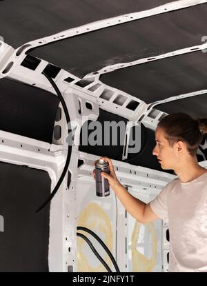 Vista verticale di un giovane uomo che utilizza una bottiglia di vernice spray per dipingere l'interno di un furgone mentre si auto-trasforma in un furgone camper Foto Stock