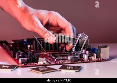 La mano di un uomo inserisce un processore nel chipset della scheda madre. Foto Stock