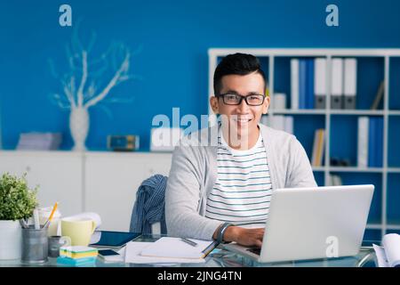 Ritratto di giovane uomo d'affari allegro che lavora su un computer portatile Foto Stock