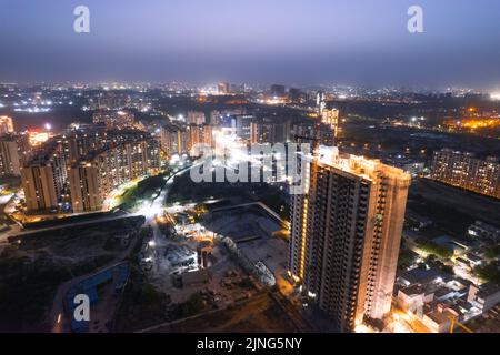 crepuscolo con droni aerei che mostra luci arancioni di strade, case e mercati che circondano un grattacielo con il paesaggio della città che si estende nel Foto Stock