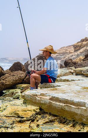 Un pescatore che tiene il gancio con la sua canna da pesca con un bellissimo tramonto nella città di Laayoune Foto Stock