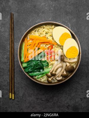 Zuppa di noodles in stile asiatico con funghi, uova, verdure assortite di dan sullo sfondo scuro. Foto Stock