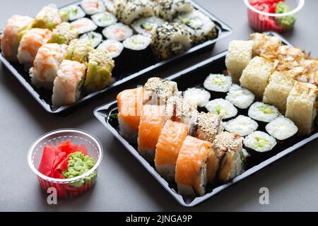 Grandi rotoli di sushi in scatola di plastica nera da portare via su sfondo grigio Foto Stock