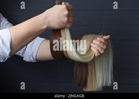 La mano maschile tiene diverse sezioni di capelli per l'estensione. Foto Stock