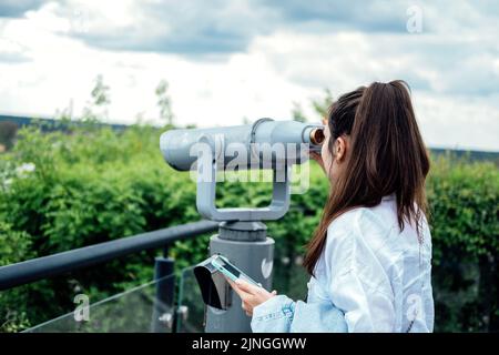 Viaggi, visite turistiche. Giovane donna turista in cerca di binocolo, telescopio Foto Stock