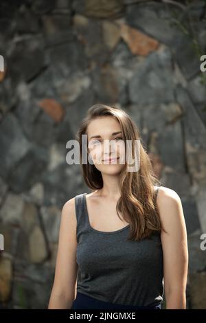 Ritratto in vita di una giovane donna naturalmente bella sorridente alla fotocamera su sfondo di pietra Foto Stock