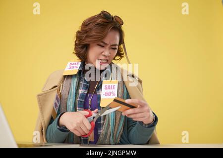 Ritratto di arrabbiata donna asiatica taglio la sua carta di credito con forbici per smettere di spendere per lo shopping Foto Stock