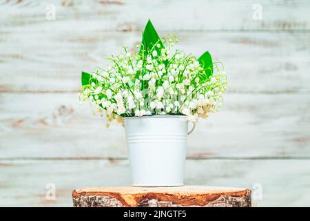 Bouquet di gigli della valle in un secchio bianco su uno sfondo di legno chiaro. Biglietto d'auguri. Messa a fuoco selettiva. Foto Stock