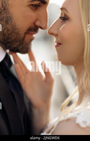 Vista laterale dell'amore felice coppia di nozze che incontra gli occhi. Giovane donna sposa toccare strofando delicatamente grooms faccia. Verticale. Foto Stock