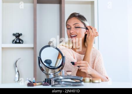 Bella donna che applica trucco (dipingere le sue ciglia) per un appuntamento serale di fronte a uno specchio. Ritratto di bella giovane donna applicando Masca Nero Foto Stock