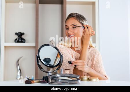 Donna brunette applicare trucco (dipingere le sue ciglia) per una data sera di fronte a uno specchio. Foto Stock