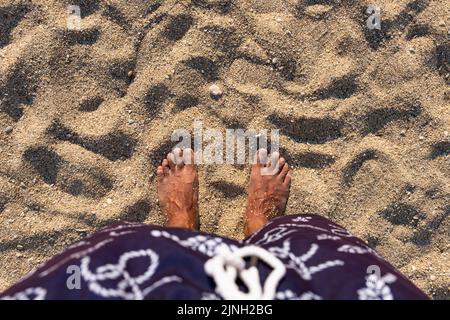 A piedi nudi in piedi sulla spiaggia. Mans piedi sulla spiaggia di sabbia. Vista dall'alto. Spazio vuoto per testo o logo Foto Stock