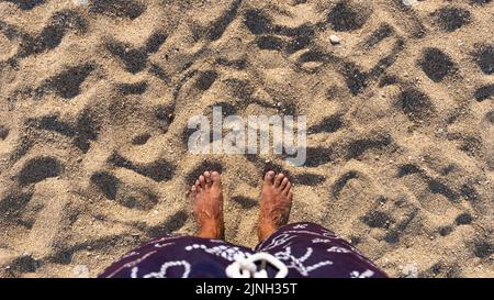A piedi nudi in piedi sulla spiaggia. Mans piedi sulla spiaggia di sabbia. Vista dall'alto. Spazio vuoto per testo o logo Foto Stock
