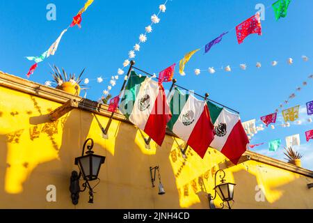 I colorati striscioni di papel picado fiesta e le bandiere messicane decorano un edificio in stile coloniale spagnolo nel centro storico di San Miguel de Allende, Messico. Foto Stock