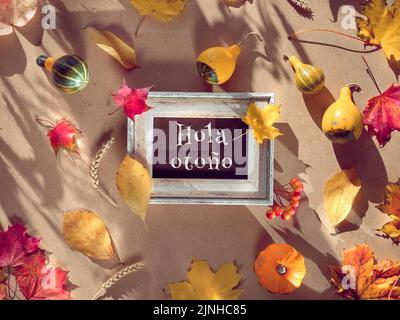 Cornice autunnale, didascalia testo di saluto Hola otono significa Hello Autunno in lingua spagnola. Foglie di caduta naturale, spighe di grano. Foto Stock