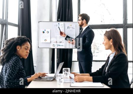 Influente caucasico attraente maschio ceo, tenendo il brainstorming di gruppo, discutendo le idee per un nuovo progetto di affari, fa una presentazione di programma di affari ai suoi soci femminili. Lavoro di squadra, collaborazione Foto Stock