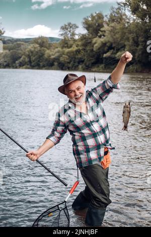 Buon vecchio pescatore pescato un pesce di trota. Ritratto di sorridente allegro uomo anziano pesca. Nonno con pesce pescato. Foto Stock