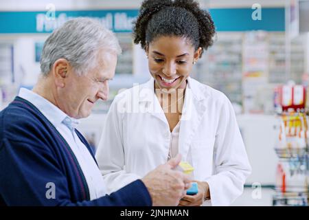 Un giovane farmacista raccomanda un prodotto sanitario a un anziano in farmacia. Foto Stock