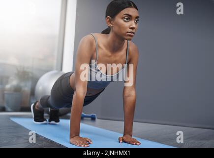 Senza nulla, gli occhi sono ancora sul premio. Una giovane donna attraente impegnata a fare esercizi di stretching sul suo tappetino da palestra a casa. Foto Stock