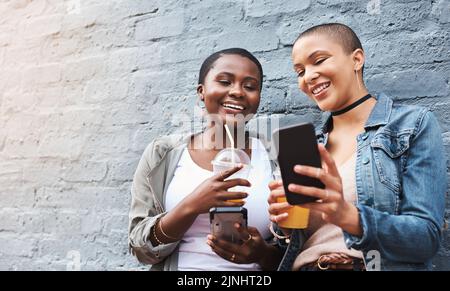 Theres sempre qualcosa di nuovo da mostrare quando youre collegato. Due giovani donne in piedi accanto a un edificio sorridendo e leggendo attraverso i messaggi di testo mentre Foto Stock