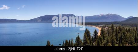 Vista panoramica del grande lago con spiaggia circondata da alberi e montagne. Foto Stock