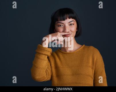 Che cosa è la vita senza un po' di sciocchia. Studio shot di una giovane donna attraente fare un baffi con il dito su uno sfondo scuro. Foto Stock