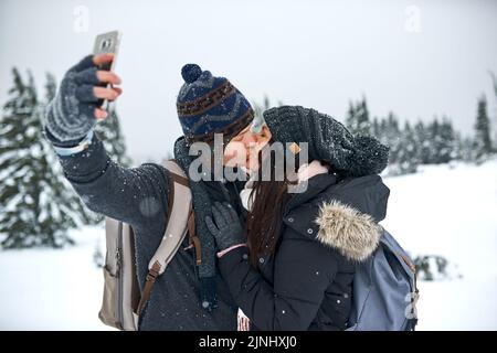 Baciami prima che le tue labbra si congelino. Un uomo che prende un selfie con la sua ragazza mentre fuori sulla neve. Foto Stock