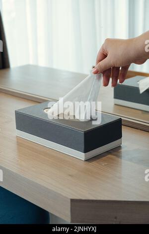 Mano donna che raccoglie carta tissue dalla scatola di carta tissue sul tavolo da trucco. Foto Stock