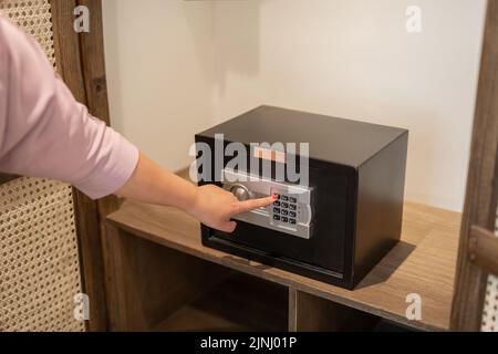 donna che inserisce il codice a mano sulla tastiera della mini cassetta di sicurezza in camera d'albergo Foto Stock