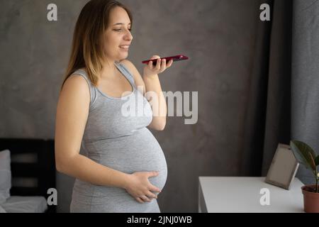 Felice giovane mamma inviare messaggio vocale record audio blog su cellulare dedicato alla maternità di anticipazione paternità paternità. Madre positiva dettare la lettera vocale a. Foto Stock