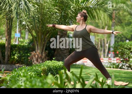 Bella donna obesa che indossa la parte superiore e i leggings in piedi sul tappetino yoga e fare esercizio stretching mentre si allenano all'aperto Foto Stock