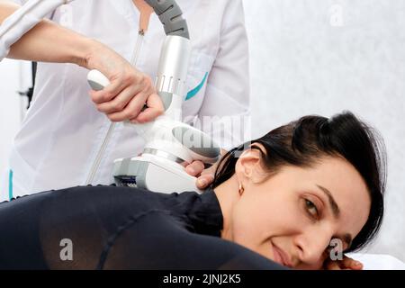 Il beautician fa il massaggio di vitello di LPG delle gambe alla donna giovane in vestito nero. Massaggio linfodrenante. Trattamenti dimagranti Foto Stock