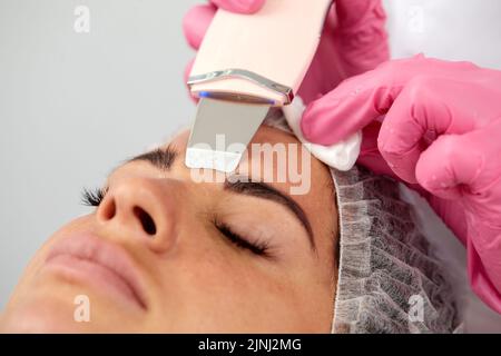 Medico di bellezza con scrabber ultrasonico che fa la procedura di pulizia ultrasonica del viso. Cosmetologia e cura della pelle del viso. Foto Stock