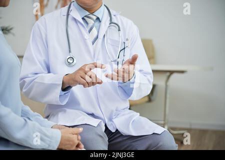 Medico altamente professionale che indossa il cappotto bianco seduto accanto alla paziente femminile e dando le sue raccomandazioni, interno di ufficio moderno sullo sfondo Foto Stock