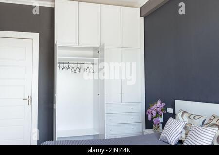 Primo piano, armadio bianco vuoto con ante aperte in una stanza grigia, copia pasta Foto Stock