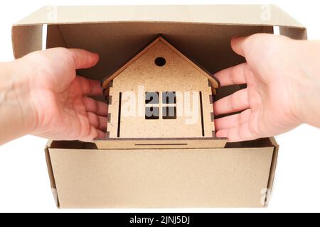 Mano che prende una casa del giocattolo di legno da una scatola di spedizione su bianco. Concetto di rilocazione creativa. Foto Stock