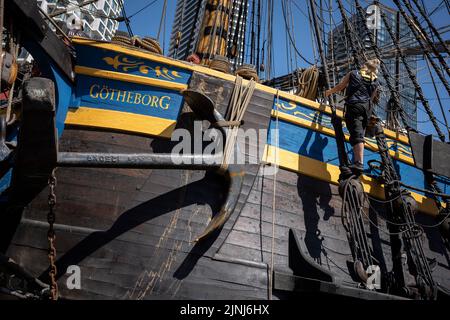 L'equipaggio della nave a vela replica, Goteborg, effettua riparazioni e manutenzione mentre attraccato sotto le alte torri di South Quay, Canary Wharf nei Docklands di Londra, durante la sua visita di quattro giorni alla capitale prima di continuare la sua spedizione di due anni intorno al mondo a Shanghai, Cina, il 9th agosto 2022, A Londra, Inghilterra. I londinesi sono invitati a visitare i ponti di questo facsimile della nave originale che affondò al largo della costa svedese nel 1745. Il suo carico principale sarebbe stato il tè, porcellana, erbe e seta sulla rotta della Cina. Foto Stock