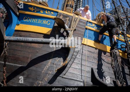 L'equipaggio della nave a vela replica, Goteborg, effettua riparazioni e manutenzione mentre attraccato sotto le alte torri di South Quay, Canary Wharf nei Docklands di Londra, durante la sua visita di quattro giorni alla capitale prima di continuare la sua spedizione di due anni intorno al mondo a Shanghai, Cina, il 9th agosto 2022, A Londra, Inghilterra. I londinesi sono invitati a visitare i ponti di questo facsimile della nave originale che affondò al largo della costa svedese nel 1745. Il suo carico principale sarebbe stato il tè, porcellana, erbe e seta sulla rotta della Cina. Foto Stock