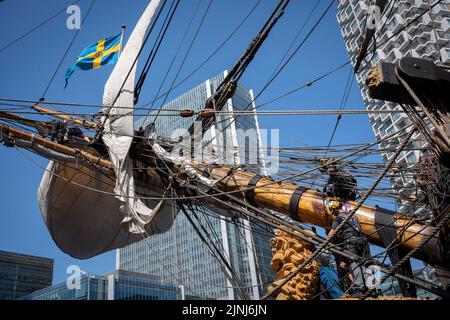 L'equipaggio della nave a vela replica, Goteborg, effettua riparazioni e manutenzione mentre attraccato sotto le alte torri di South Quay, Canary Wharf nei Docklands di Londra, durante la sua visita di quattro giorni alla capitale prima di continuare la sua spedizione di due anni intorno al mondo a Shanghai, Cina, il 9th agosto 2022, A Londra, Inghilterra. I londinesi sono invitati a visitare i ponti di questo facsimile della nave originale che affondò al largo della costa svedese nel 1745. Il suo carico principale sarebbe stato il tè, porcellana, erbe e seta sulla rotta della Cina. Foto Stock