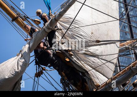 L'equipaggio della nave a vela replica, Goteborg, effettua riparazioni e manutenzione mentre attraccato sotto le alte torri di South Quay, Canary Wharf nei Docklands di Londra, durante la sua visita di quattro giorni alla capitale prima di continuare la sua spedizione di due anni intorno al mondo a Shanghai, Cina, il 9th agosto 2022, A Londra, Inghilterra. I londinesi sono invitati a visitare i ponti di questo facsimile della nave originale che affondò al largo della costa svedese nel 1745. Il suo carico principale sarebbe stato il tè, porcellana, erbe e seta sulla rotta della Cina. Foto Stock