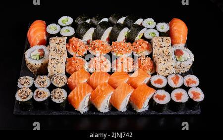 Assortimento di diversi tipi di sushi a rullo disposti su un pannello di pietra nera. Menu sushi con nigiri, maki, uramaki da ordinare in un ristorante o deli Foto Stock