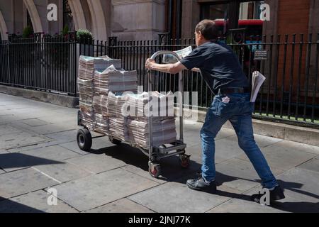 Un venditore di giornali standard di sera spinge un carrello pieno di copie di primavera nella City of London, il quartiere finanziario della capitale (noto anche come Square Mille), il 10th agosto 2022, a Londra, Inghilterra. Foto Stock