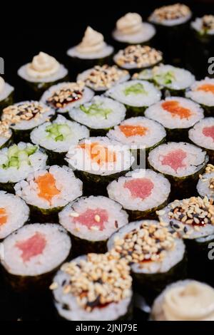 Grande set di panini Maki con una varietà di ripieni di pesce fresco e verdure. Panini con formaggio cremoso, salmone, cetriolo, semi di sesamo e salsa. Selezionare Foto Stock