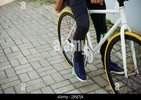 Primo piano di un uomo irriconoscibile in bicicletta lungo la strada della città illuminata da raggi di sole Foto Stock