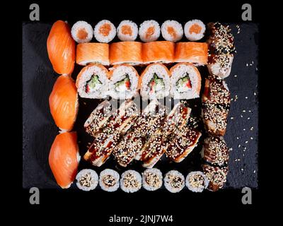 Cucina giapponese orientale. Vista dall'alto di un grande set di sushi su una tavola di pietra nera. Molti maki, nigiri e panini diversi. Concetto di consegna di d Foto Stock