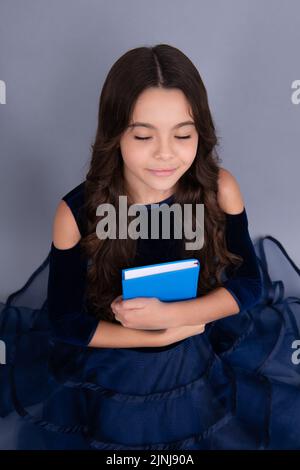 Sognando la scolaretta in vestire tenere un libro e copybook pronti per imparare. I bambini della scuola sognano su un fondo grigio isolato. Foto Stock